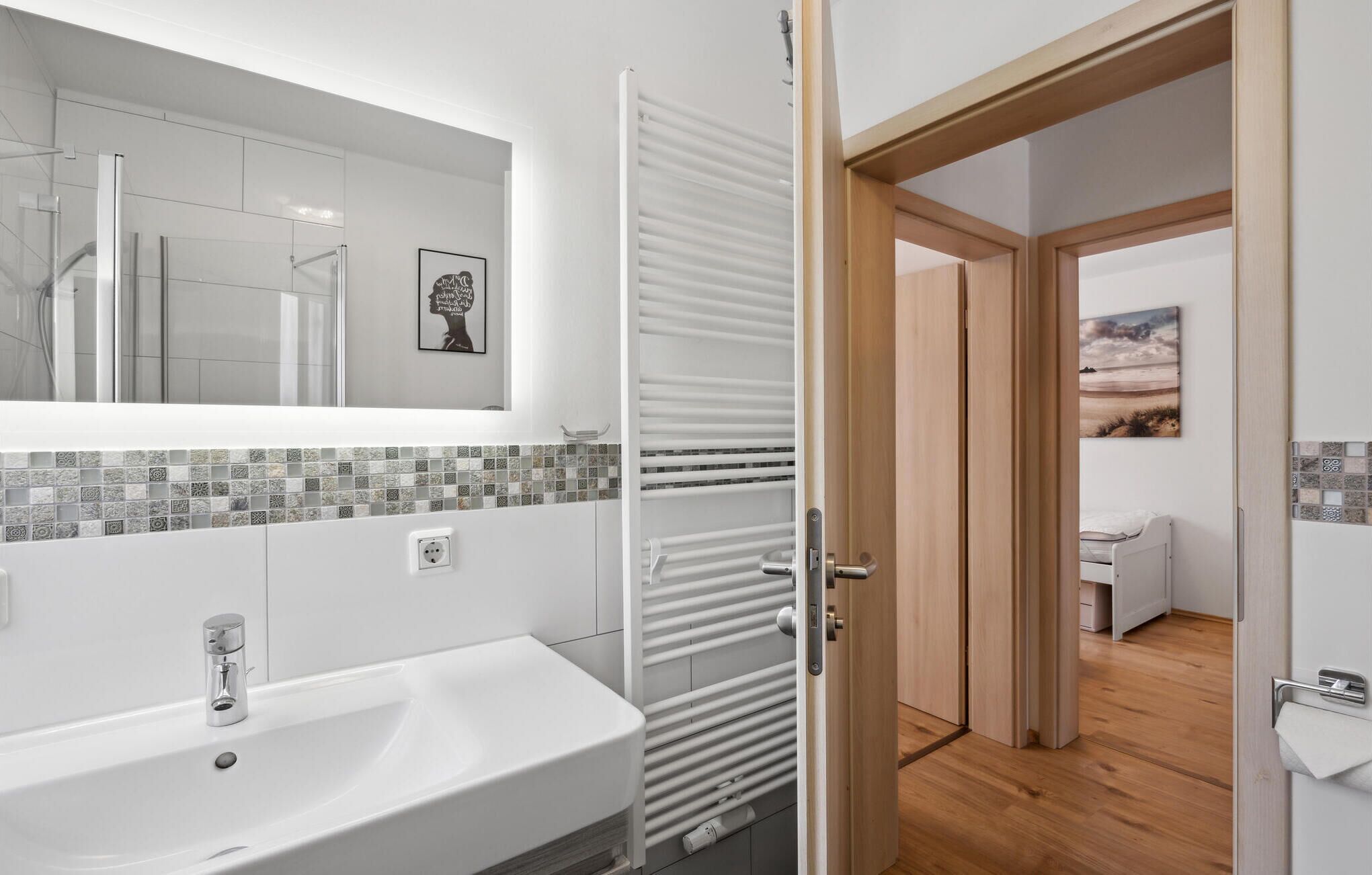 A modern bathroom with a white sink, a mirror, and a tiled backsplash.