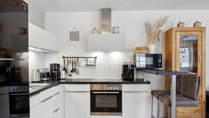 A modern kitchen with white cabinetry, a built-in oven, a coffee maker, and a microwave. - Ferienhaus 31 Altefähr (Altefähr/Rügen)
