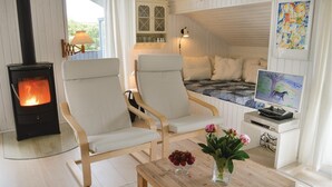 Une pièce chaleureuse avec une cheminée, deux fauteuils, un lit avec vue, une télévision et une table décorée de fleurs.