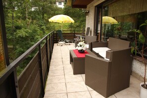 Un balcon agrémenté de meubles en osier, d’une table rouge et de deux parasols jaunes.