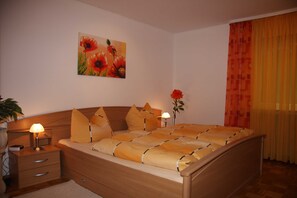 A bedroom with a wooden bed, bedside lamps, a nightstand, a wall-mounted painting, and a window with curtains.