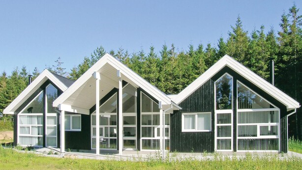 Una hilera de cabañas modernas con ventanas amplias y detalles blancos, ubicadas en un área boscosa.