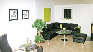 Una sala de estar moderna con un sofá seccional negro, una mesa de centro redonda y una planta en maceta. Hay dos cuadros en la pared y una puerta verde.
