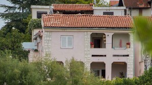 Ein Küstenhaus mit Ziegeldach, einem Balkon mit Blumentöpfen und einem Sandstrand im Vordergrund.