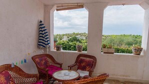 Ein überdachter Patio-Bereich mit Korbmöbeln, einem kleinen Tisch und Blumentöpfen.