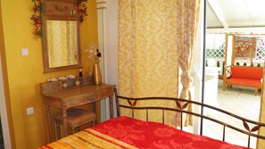 Une chambre avec un lit, une commode en bois, un miroir et une vue sur un espace extérieur aménagé avec une chaise.