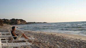 Una playa con sillas de descanso blancas y una persona sentada en una de ellas.