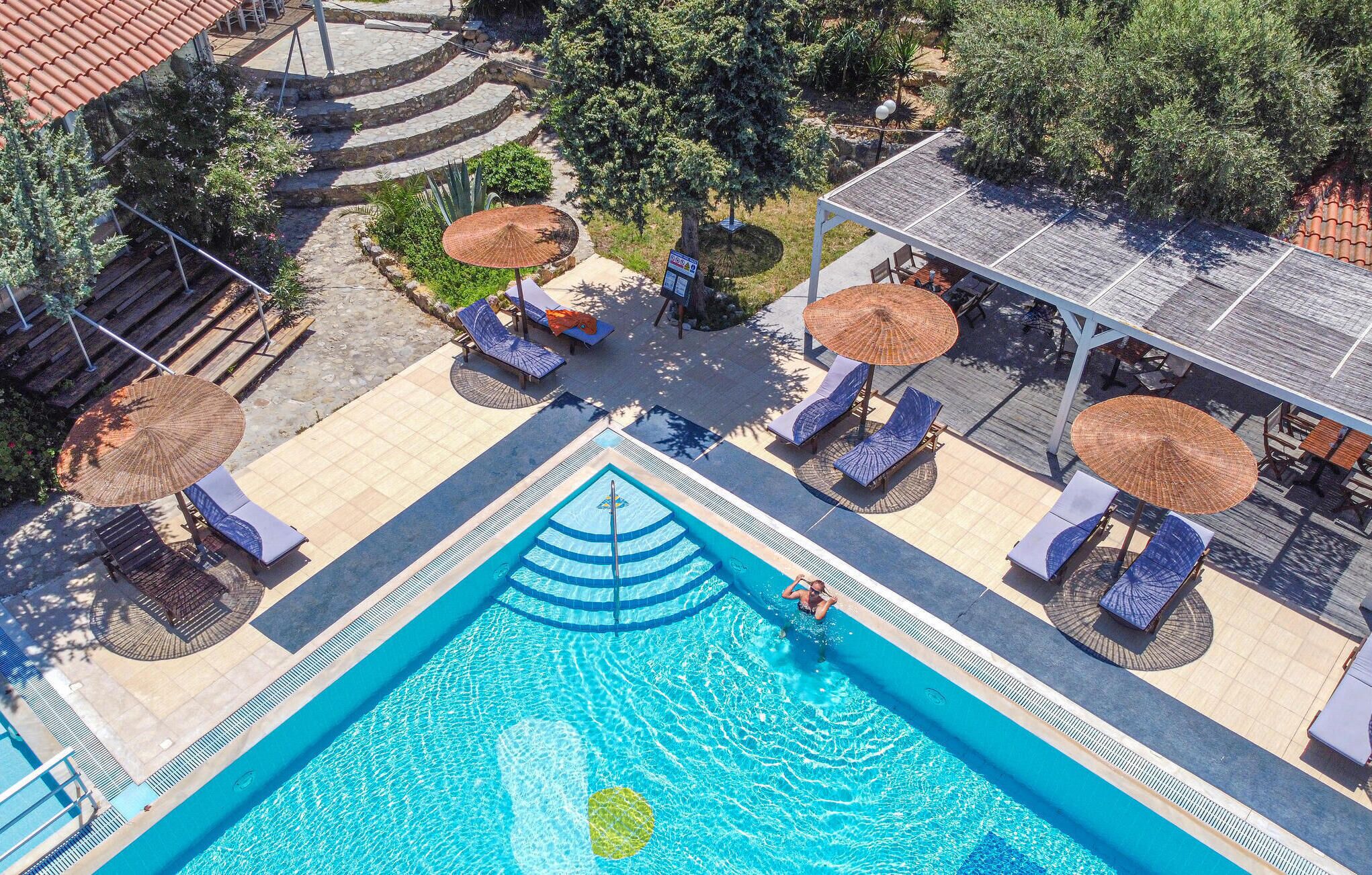 Une piscine sur le toit, agrémentée de chaises longues et de parasols, entourée d’un jardin aménagé et d’une terrasse carrelée.