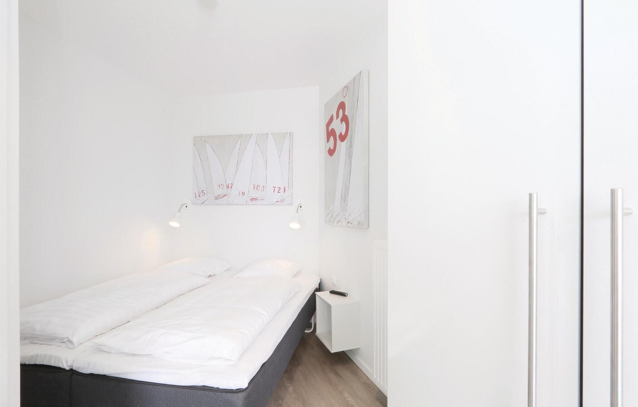 A small, clean room with a bed, a nightstand, and a wall-mounted light fixture.