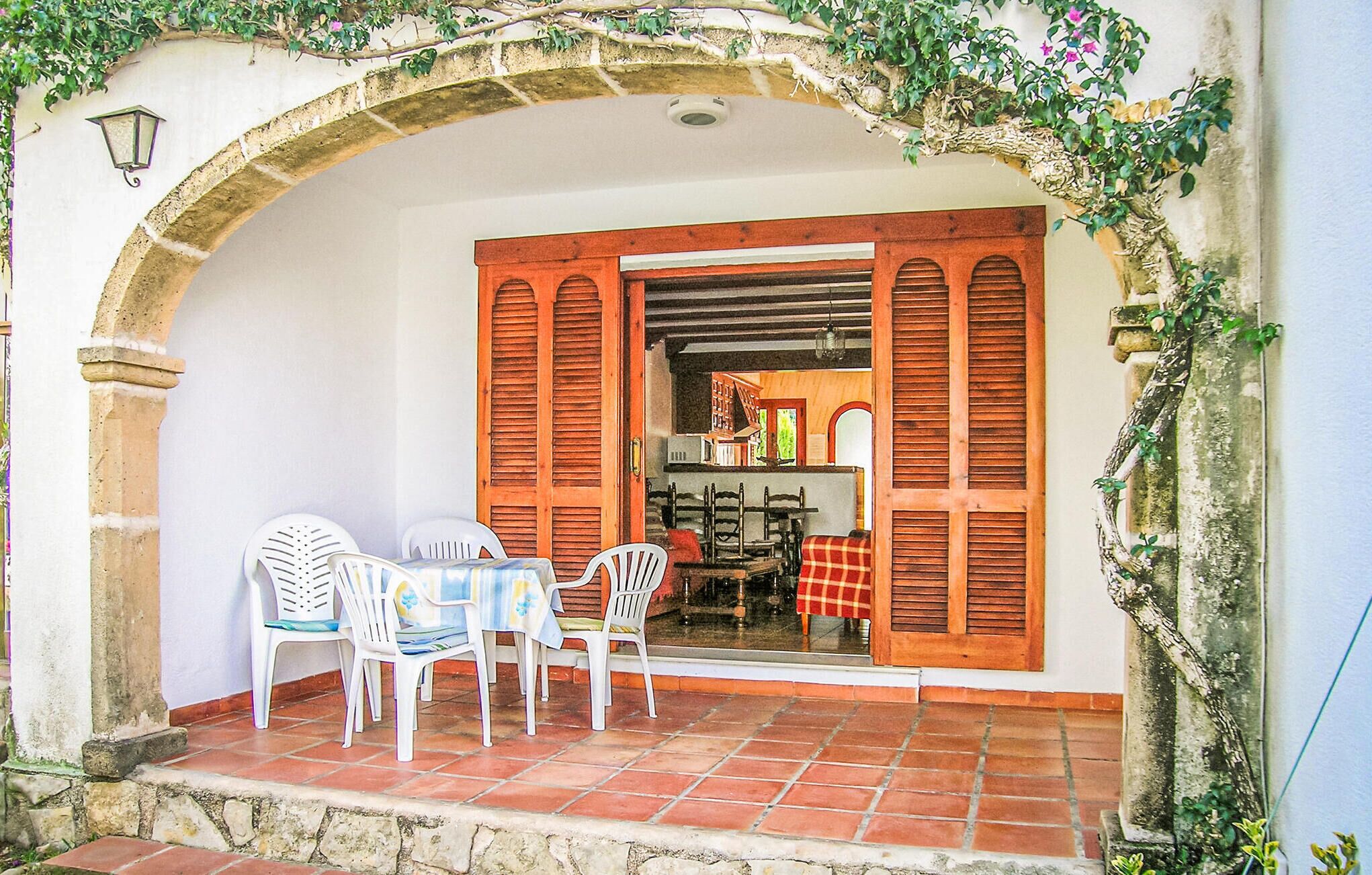 An outdoor patio with a table and chairs, a stone archway, and wooden shutters.