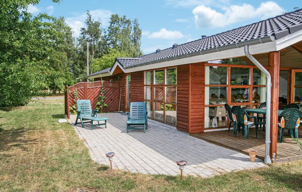 A wooden house with a tiled roof, a covered patio with chairs and a table, and a fenced garden area.