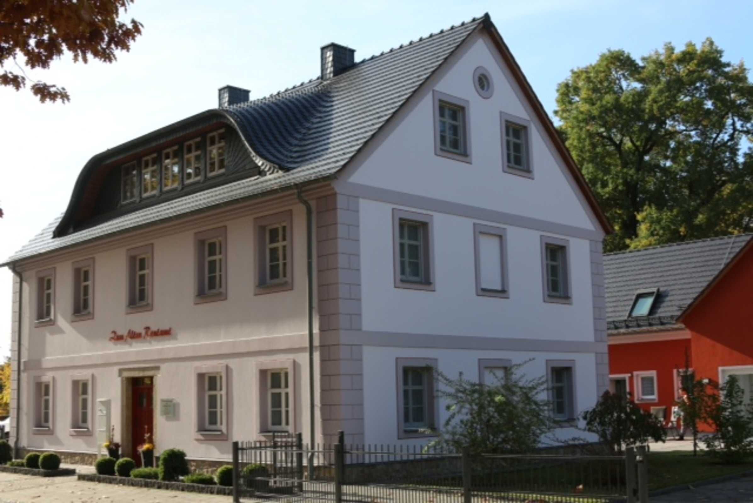 A two-story building with a white facade, multiple windows, and a red door.