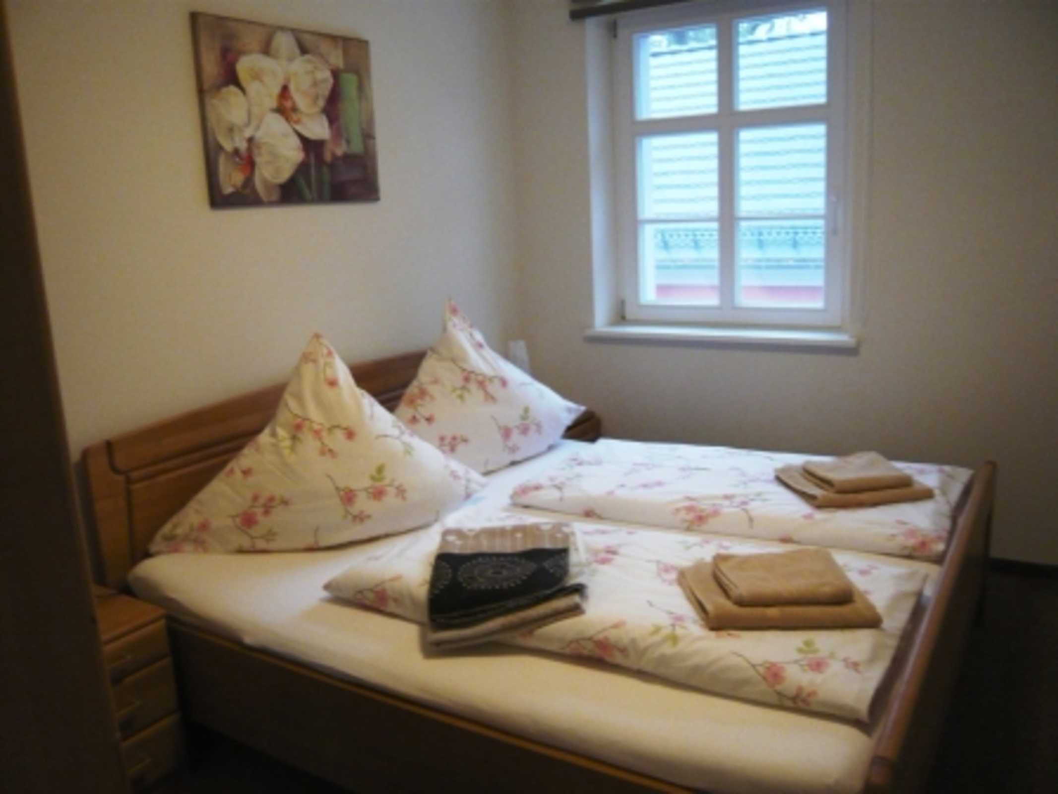 A neatly made bed with floral bedding, pillows, and folded towels.