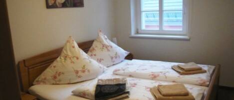 A neatly made bed with floral bedding, pillows, and folded towels.