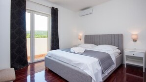A bedroom with a bed, a nightstand, a lamp, and a view of greenery through the window.