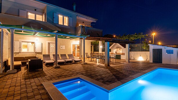 A pool area with a built-in pool, lounge chairs, and a covered seating area with tables and chairs.