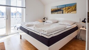 Una camera da letto moderna con un letto grande, vista sull'esterno attraverso una porta scorrevole in vetro e un quadro sopra il letto.