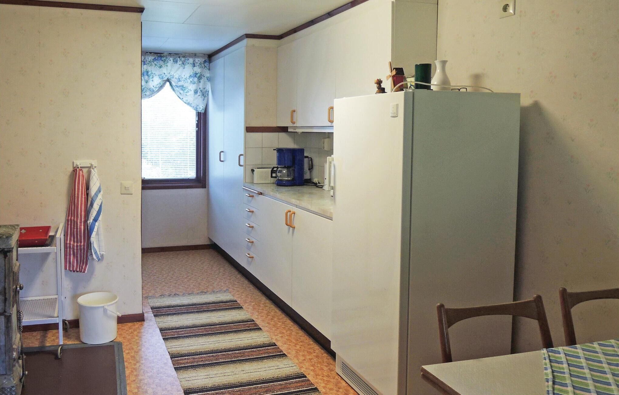 A compact kitchen with a refrigerator, a coffee maker, and a window with curtains.