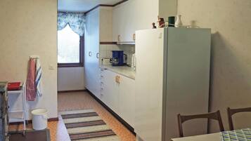 A compact kitchen with a refrigerator, a coffee maker, and a window with curtains.