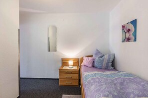 A bedroom with a bed, a nightstand with a lamp, a wall-mounted mirror, and a painting. - Holiday apartment with shared balcony (Todtmoos)