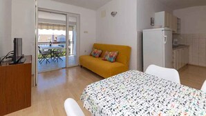 Una habitación con cama, sofá, mesa de comedor, zona de cocina y puerta corrediza de vidrio que da a un patio exterior.