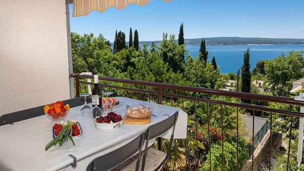 Un balcón con una mesa lista para comer, con vista a un paisaje que incluye agua y follaje.