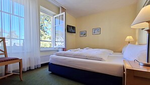 A hotel room with a bed, a chair, a window with curtains, a lamp, and two framed pictures on the wall. - Vacation apartment 1.1.10 Inselstrand - Holiday apartment 1.1.10 Lottchen (Heringsdorf)