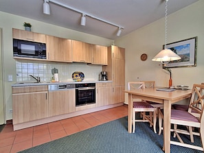 Une cuisine compacte dotée de meubles en bois, d’un four à micro-ondes, d’une machine à café et d’une table à manger avec des chaises.