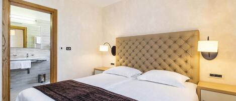 A hotel room with a large bed, two bedside tables, a headboard, and a bathroom visible through an open door.