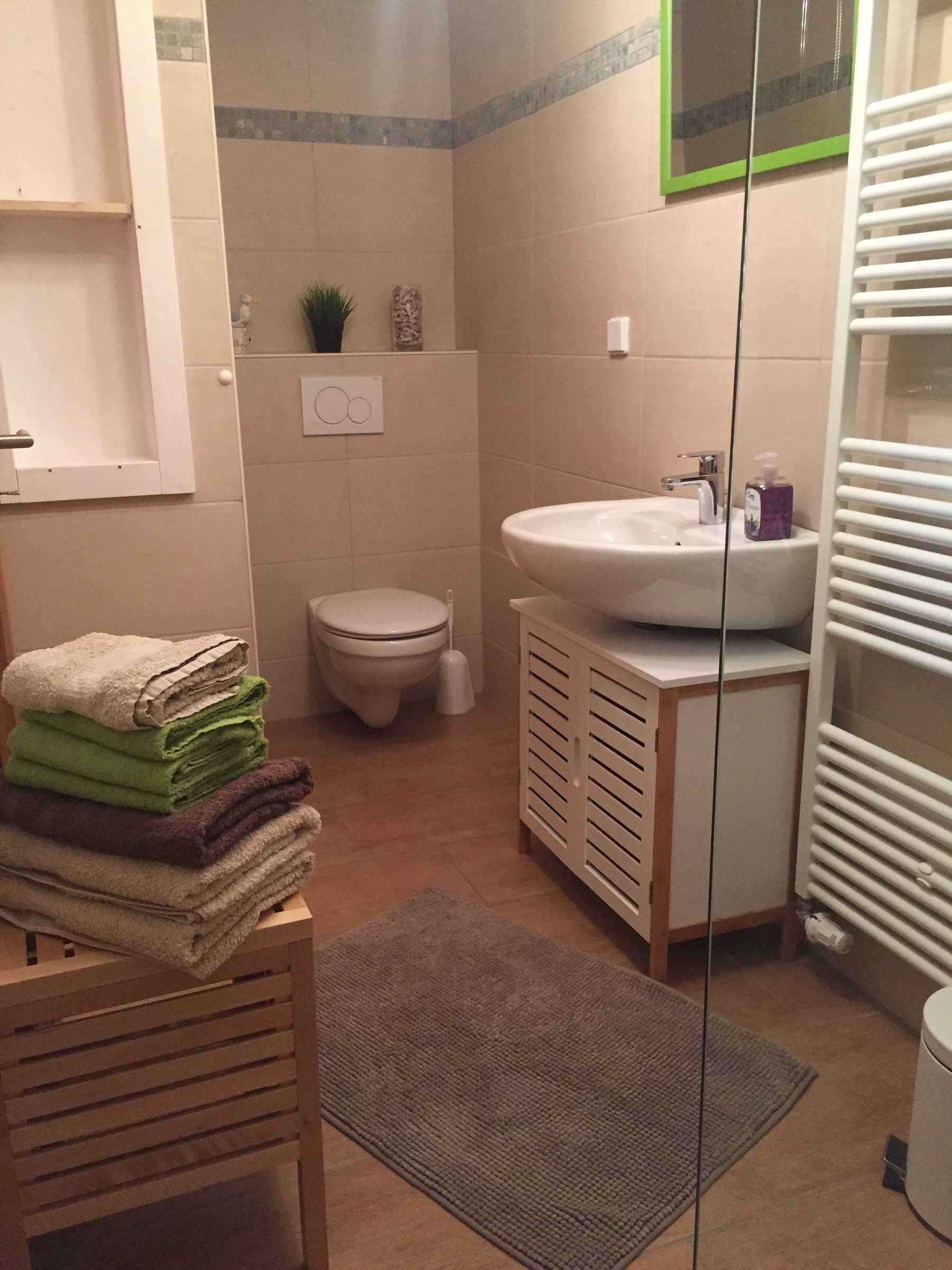 A small bathroom with a toilet, sink, and a stack of folded towels on a wooden stool.