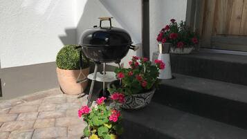Un barbecue, des plantes en pot et des marches menant à une porte en bois.