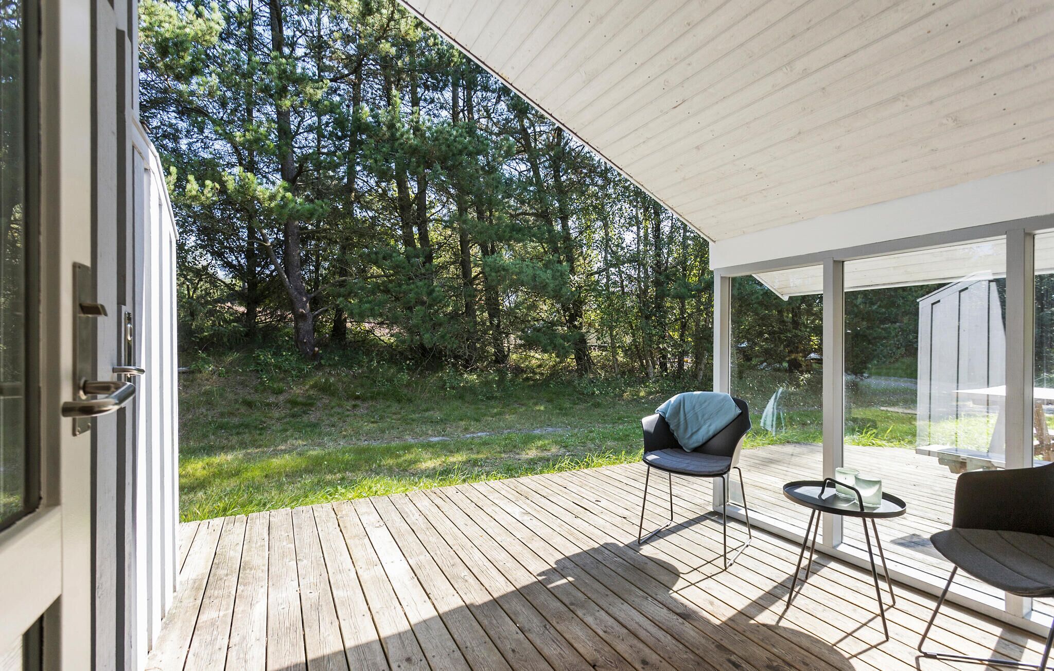 Une terrasse ouverte avec une chaise et une petite table, donnant sur une zone boisée.