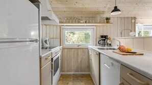 Une cuisine de taille réduite, dotée d’appareils électroménagers blancs, d’une fenêtre et d’un plafond en bois.