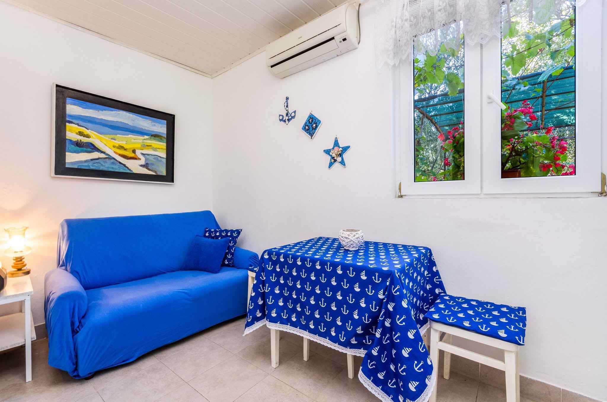 A room with a blue sofa, a table with a blue tablecloth, and a painting on the wall.