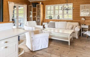 Un interior de cabaña acogedor, con un sofá blanco, una mesa de comedor y una estantería.