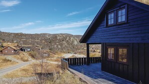 Une cabane en bois sombre, dotée d’un porche donnant sur un paysage rural.