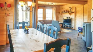 Un intérieur en bois comprenant une table à manger, des chaises, un lustre, un téléviseur et une cheminée.