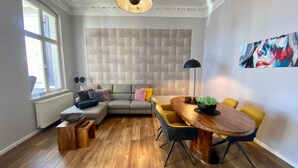 Ein modernes Wohnzimmer mit einem Ecksofa, einem Holzesstisch mit gelben Stühlen, einer schwarzen Stehlampe und einem großen abstrakten Gemälde an der Wand.