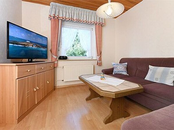 A living room with a television, a sofa, a wooden cabinet, and a window with curtains.