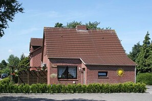 A two-story brick house with a sloped roof, a small garden, and a wooden fence.