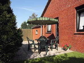 A patio with a table and chairs, a green checkered umbrella, and a brick building in the background.