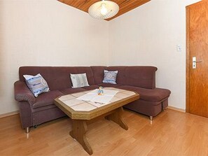 A room with a wooden ceiling, a brown sofa with cushions, and a wooden coffee table.