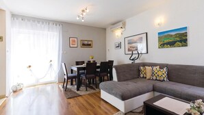 A living room with a sofa, a dining table with chairs, and a kitchen area with an air conditioner. - Amazing apartment in Bacinska jezera (Bacinska jezera)
