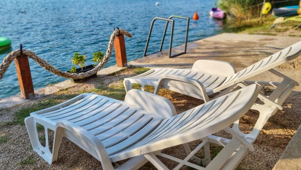 A lakeside setting with white lounge chairs and a rope swing. - Amazing apartment in Bacinska jezera (Bacinska jezera)