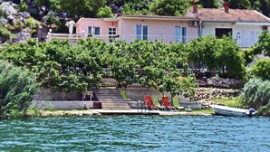 A coastal house with a stone staircase leading to a deck, surrounded by lush greenery and a calm sea. - Amazing apartment in Bacinska jezera (Bacinska jezera)