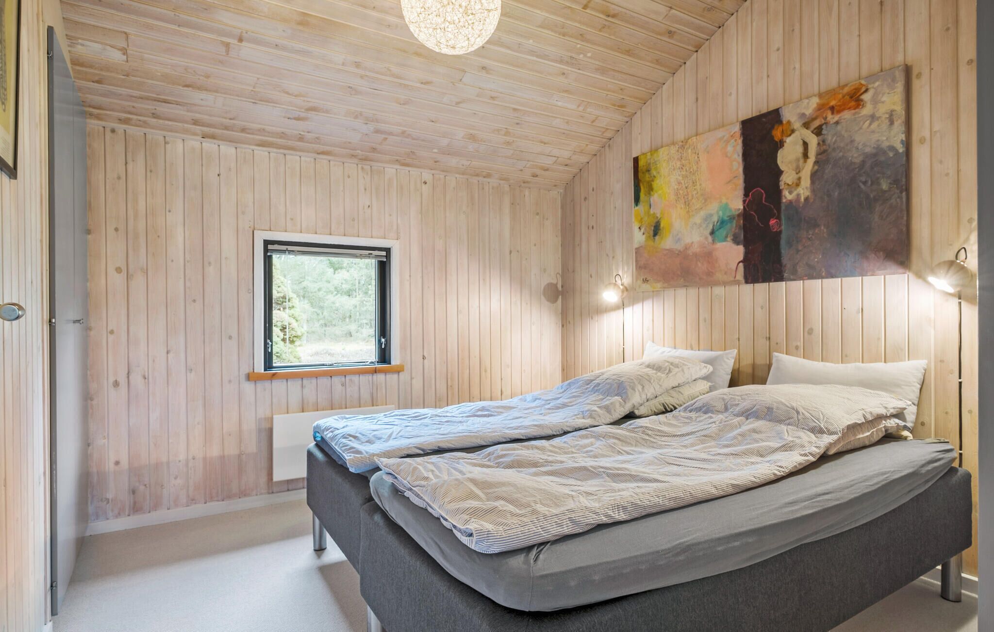 Een slaapkamer met een groot bed, houten wanden, een raam en een kleurrijk abstract schilderij.