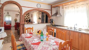 A dining area with a table set for four, a kitchen with a stove and sink, and a living room with a sofa and a TV. - 3 bedroom cozy home in Torrox (Torrox)