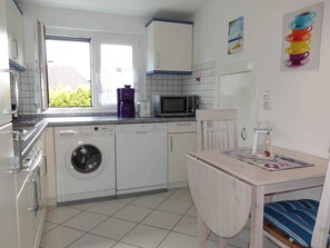 A compact kitchen with a washing machine, microwave, and a small dining area with a table and chair.