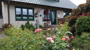 Une maison avec une porte verte, un toit en tuiles et un jardin où poussent des fleurs roses.