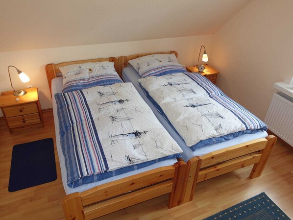A wooden bed with a striped bedspread and two pillows, flanked by nightstands with lamps, in a room with wooden flooring and a radiator.